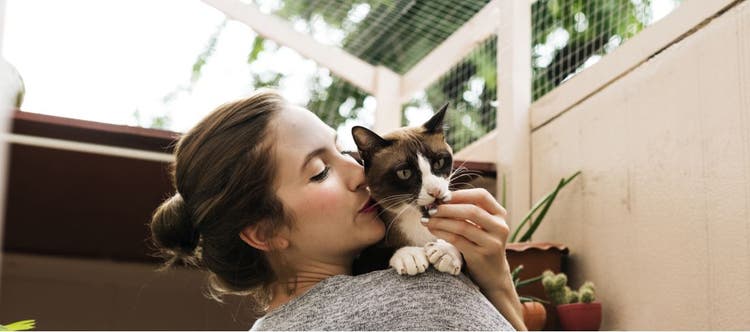 A woman and her cat embrace on the patio.
