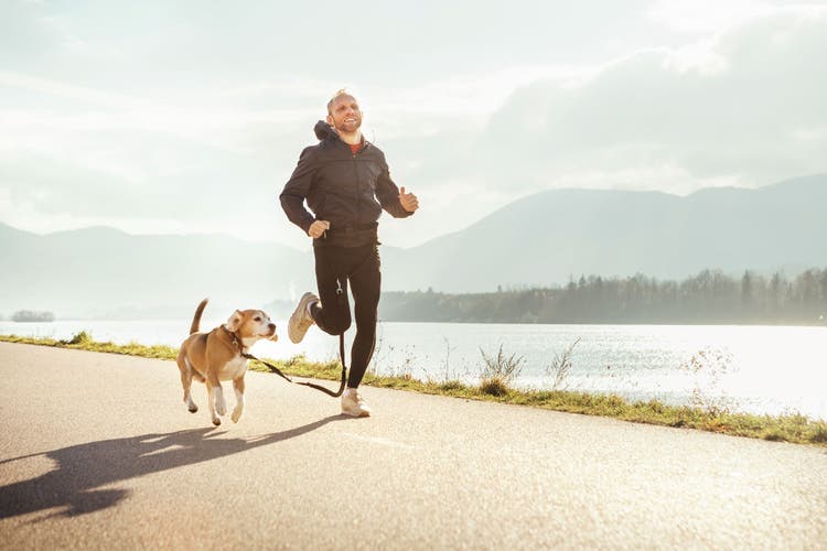A man in a black tracksuit jogs with his dog.