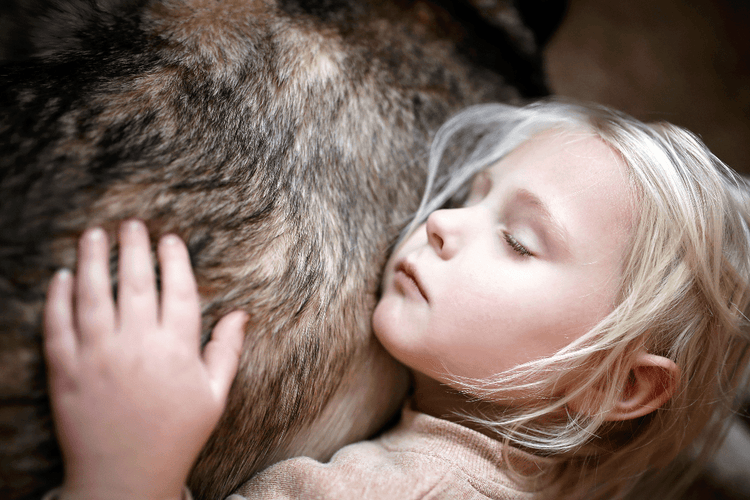 A child rests with her head against a dog's fur.