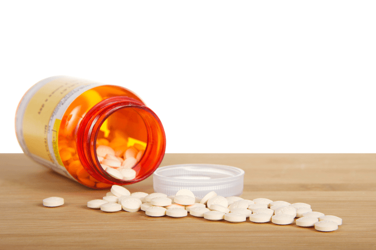 Cimetidine HCl pills for dogs and cats pouring out of an orange bottle onto a wooden table.