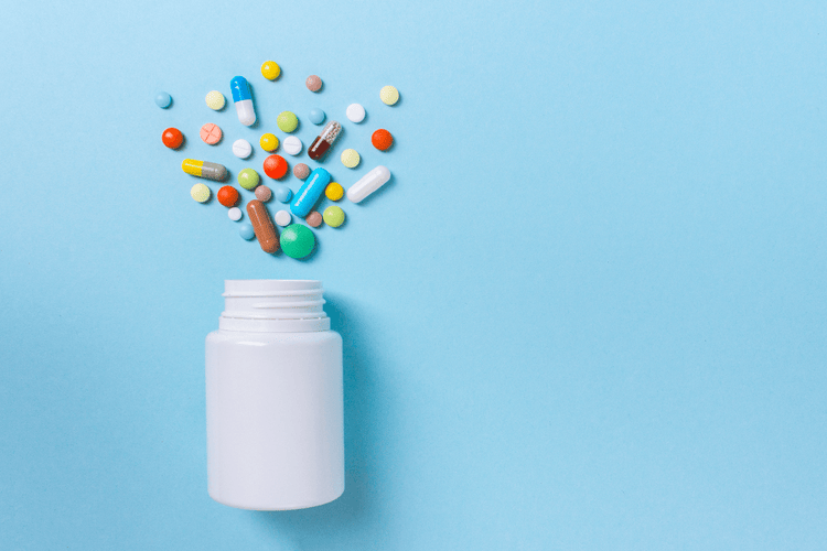A collection of multi-colored pills assorted around a white bottle on a blue table.