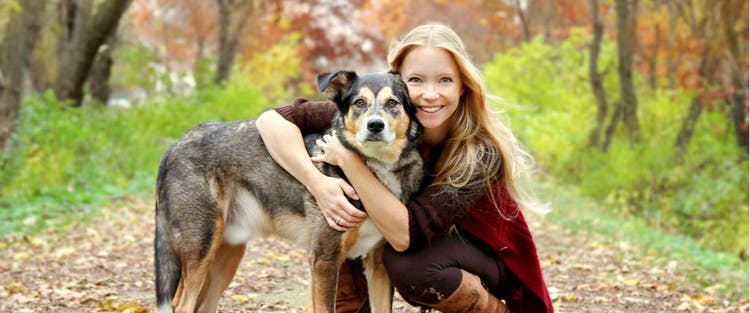 A woman and her dog stop for a hug on a leafy trail.