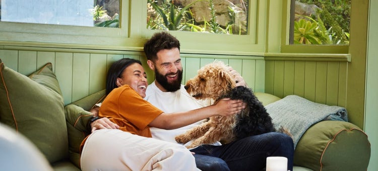 A person and person sitting on a couch with a dog Description automatically generated