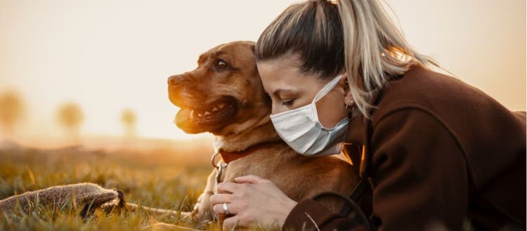 A woman in a face mask and her dog lounge in the park.