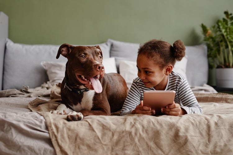 young girl smiling at her dog while they lay next to each other