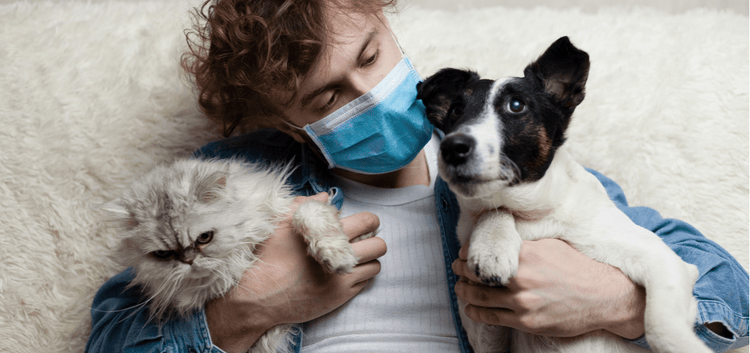 A man in a face mask holding his cat and dog.