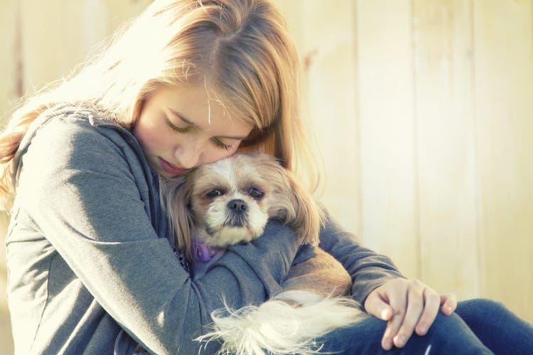 A sad teenager hugs her dog.
